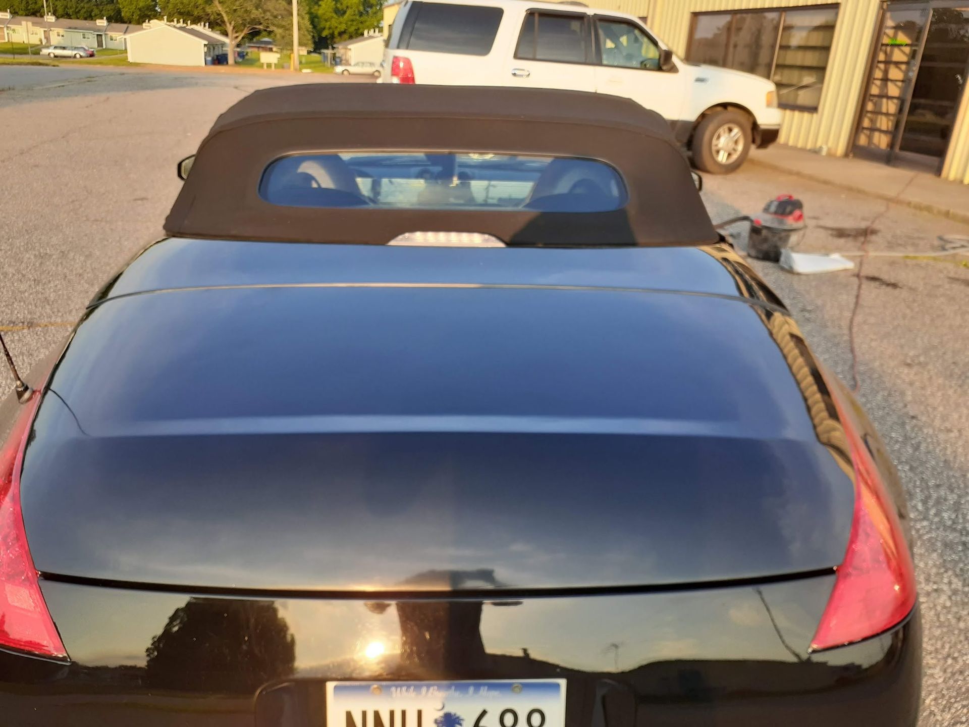Black convertible car parked outdoors, viewed from the rear with a beige pickup truck in the background.