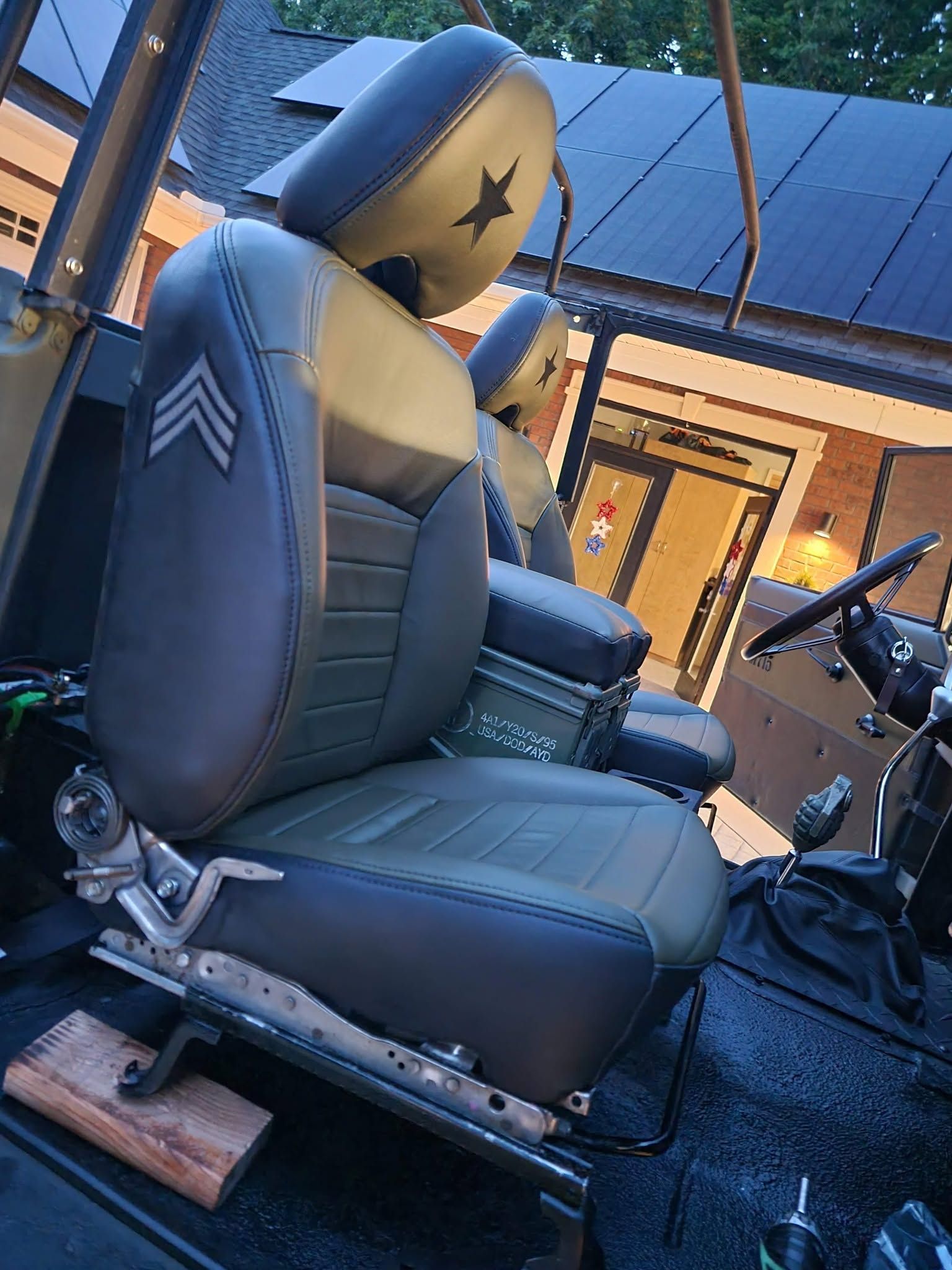 Car seat-like upholstered chair inside a workshop, mounted on a metal base with tools nearby.