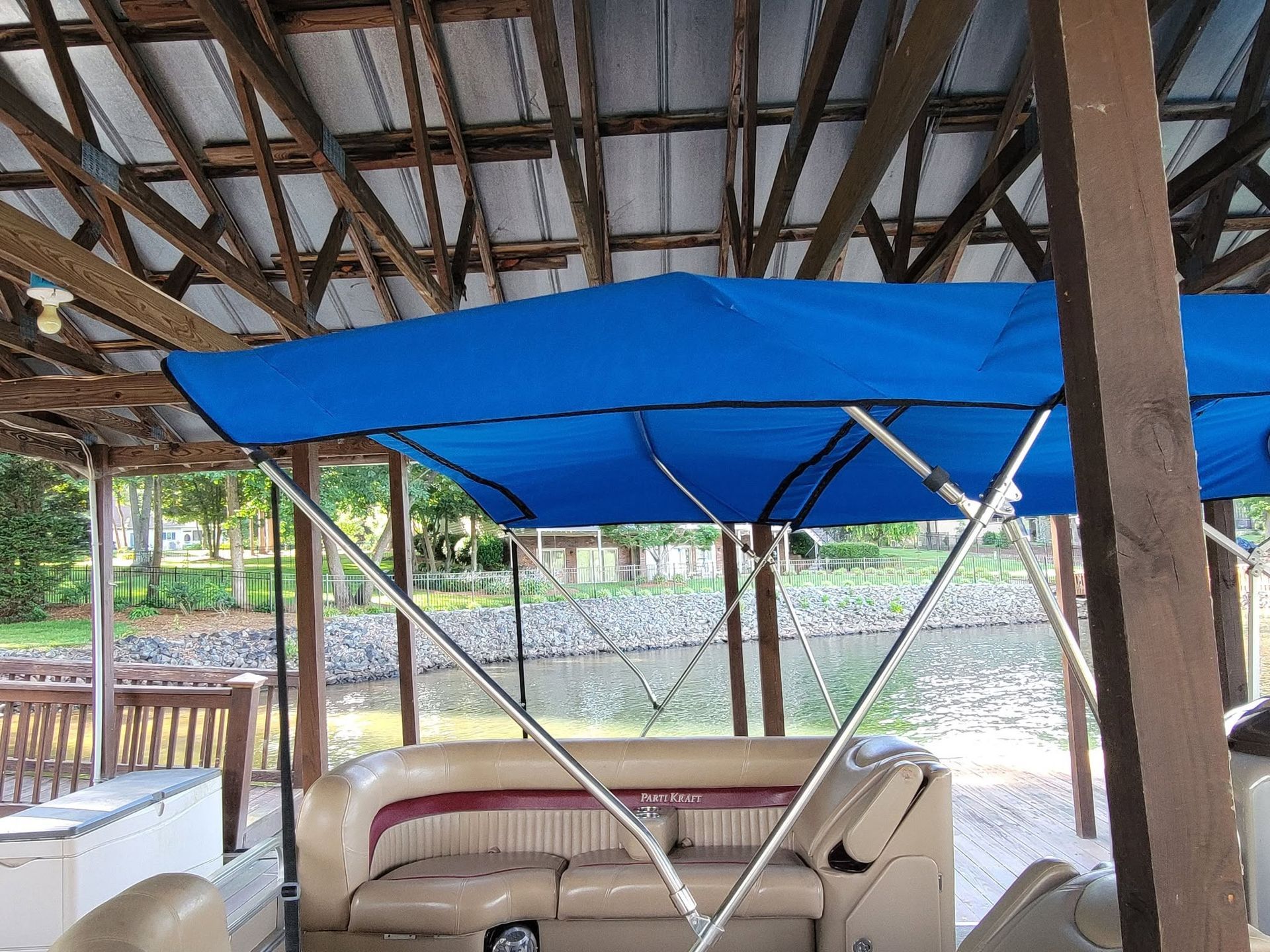 Blue-canopied outdoor seating area with a beige couch under a wooden roof by the water