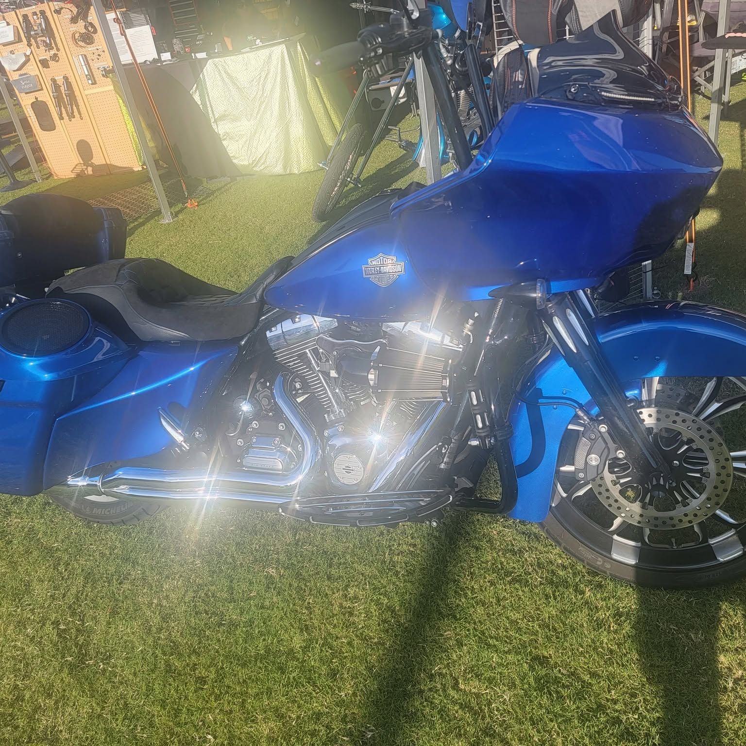 Blue motorcycle parked on grass in bright sunlight, with chrome engine and black seats