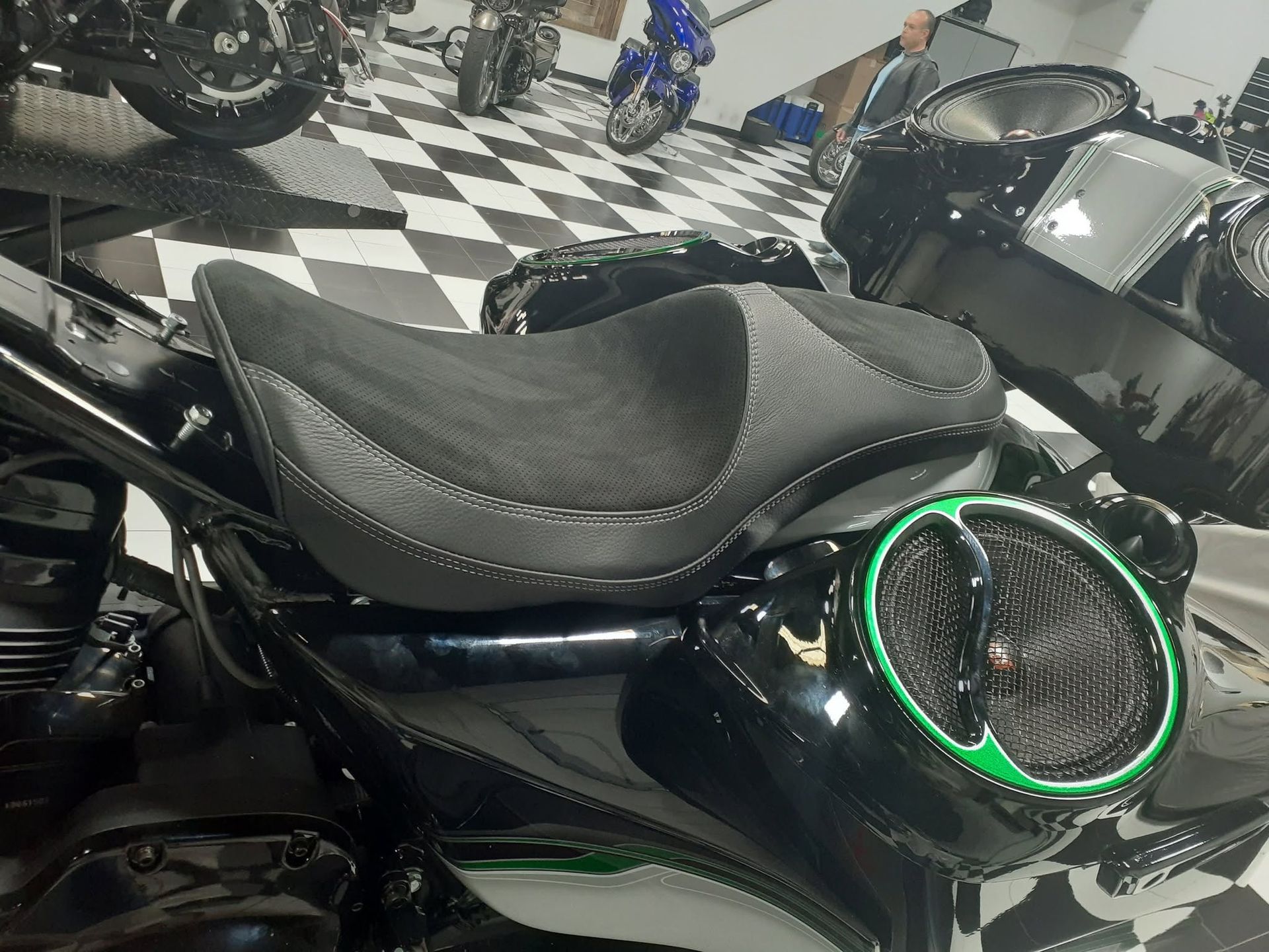 Black motorcycle with stitched seat and neon green-rimmed speaker in a showroom on checkered floor