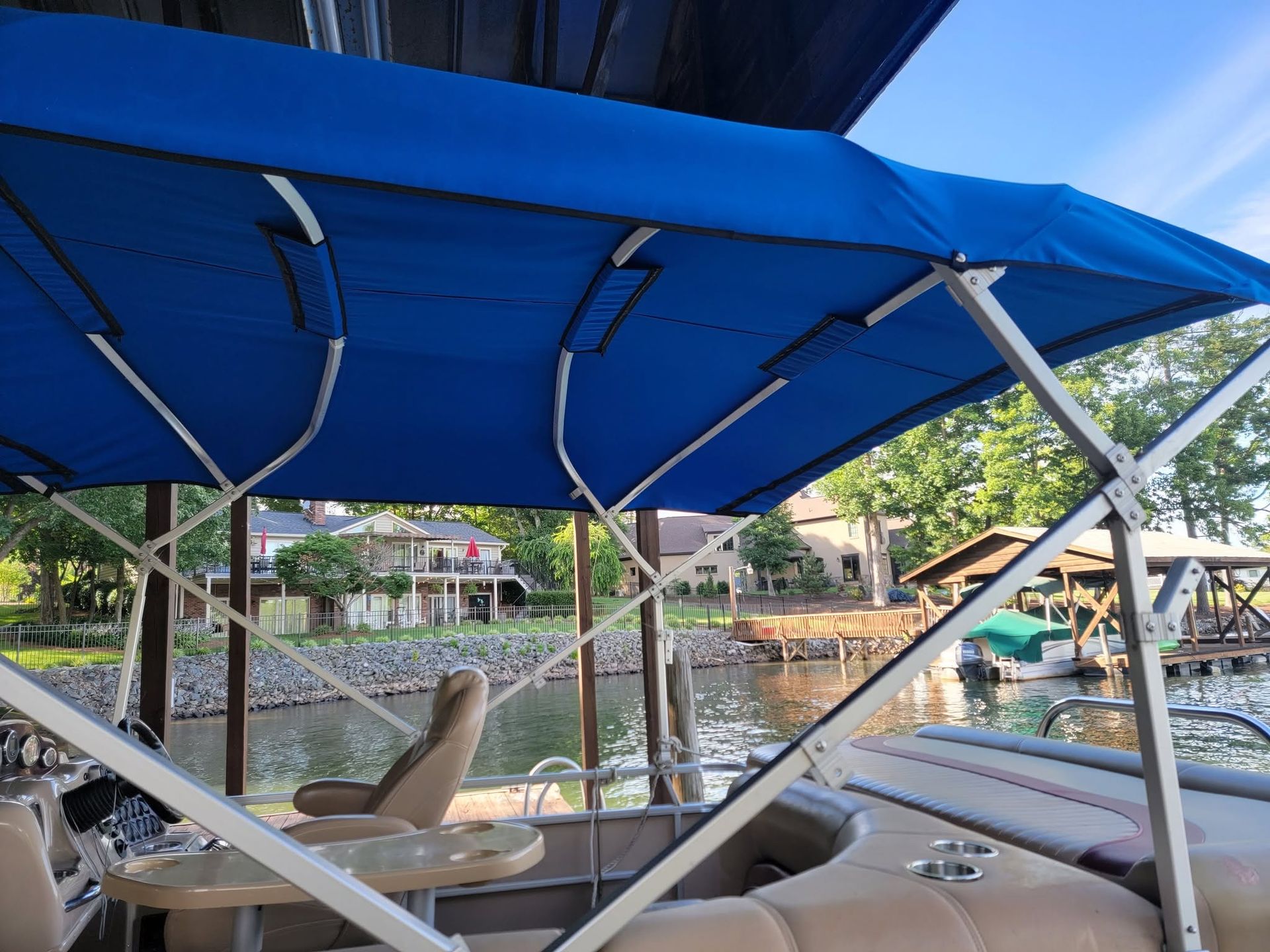 Blue canopy on a boat docked by a calm waterfront with homes and trees in the background