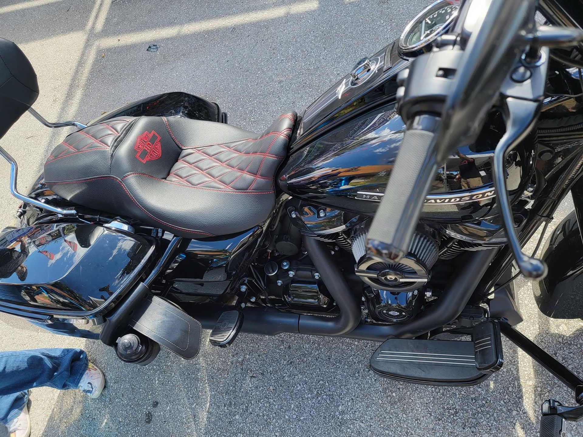 Black motorcycle parked on asphalt, viewed from above, with a red patterned seat and chrome details