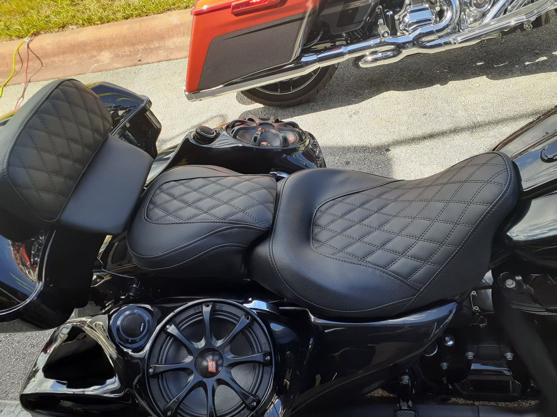 Black motorcycle with quilted seats parked by a curb, with a red vehicle in the background