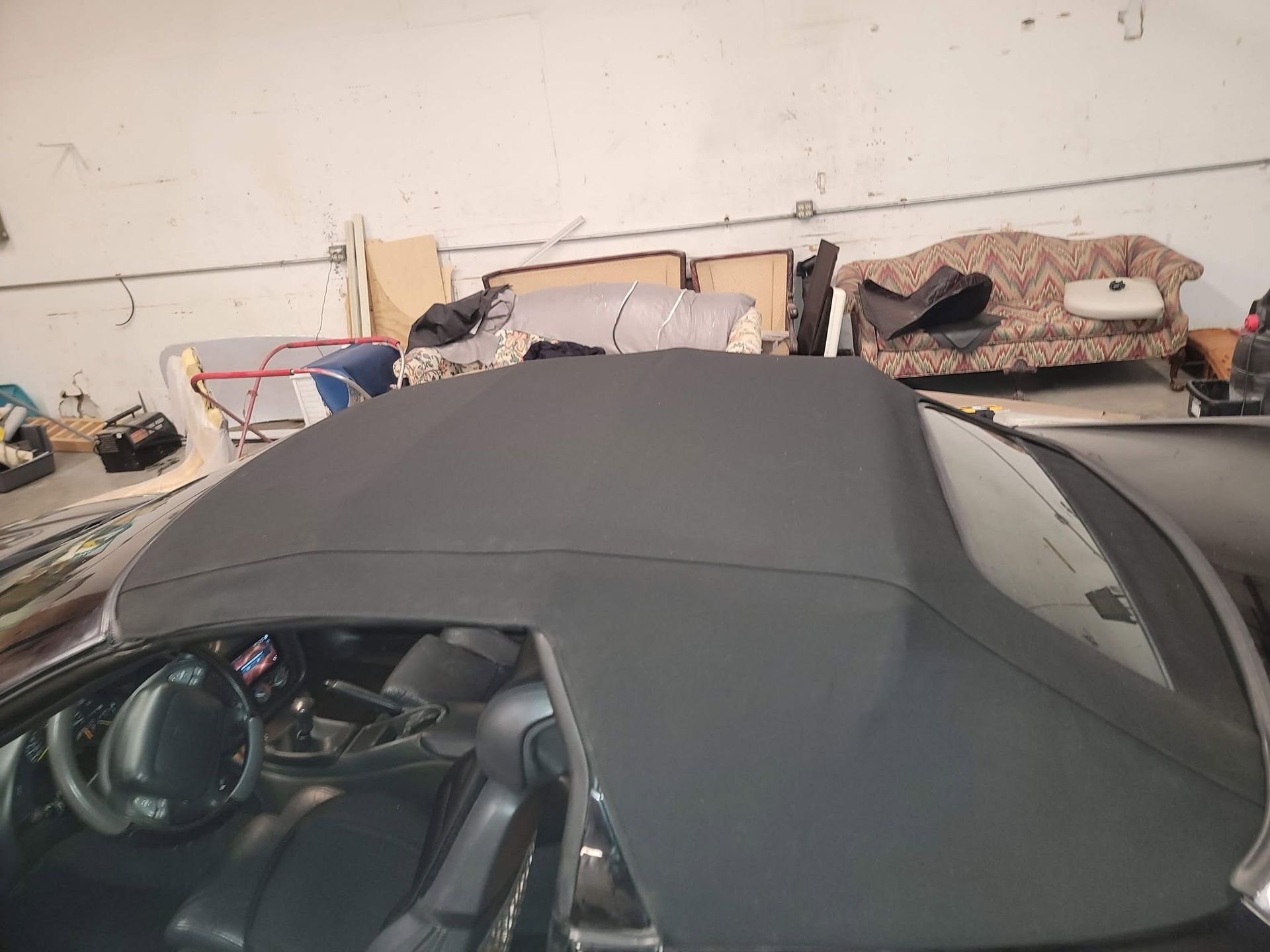 Black convertible with soft top in a cluttered garage with boxes and tools behind it