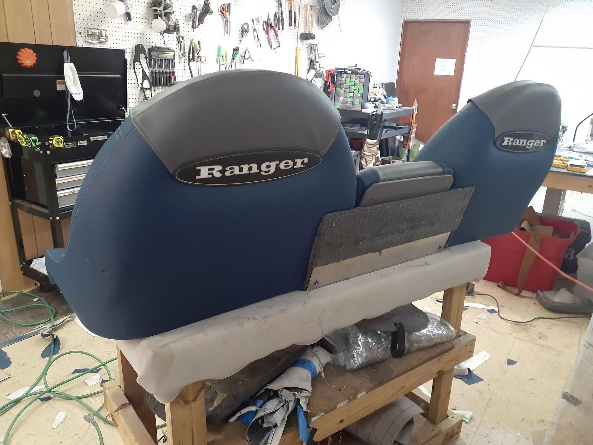 Two blue Ranger boat seats in a workshop, with tools and clutter in the background