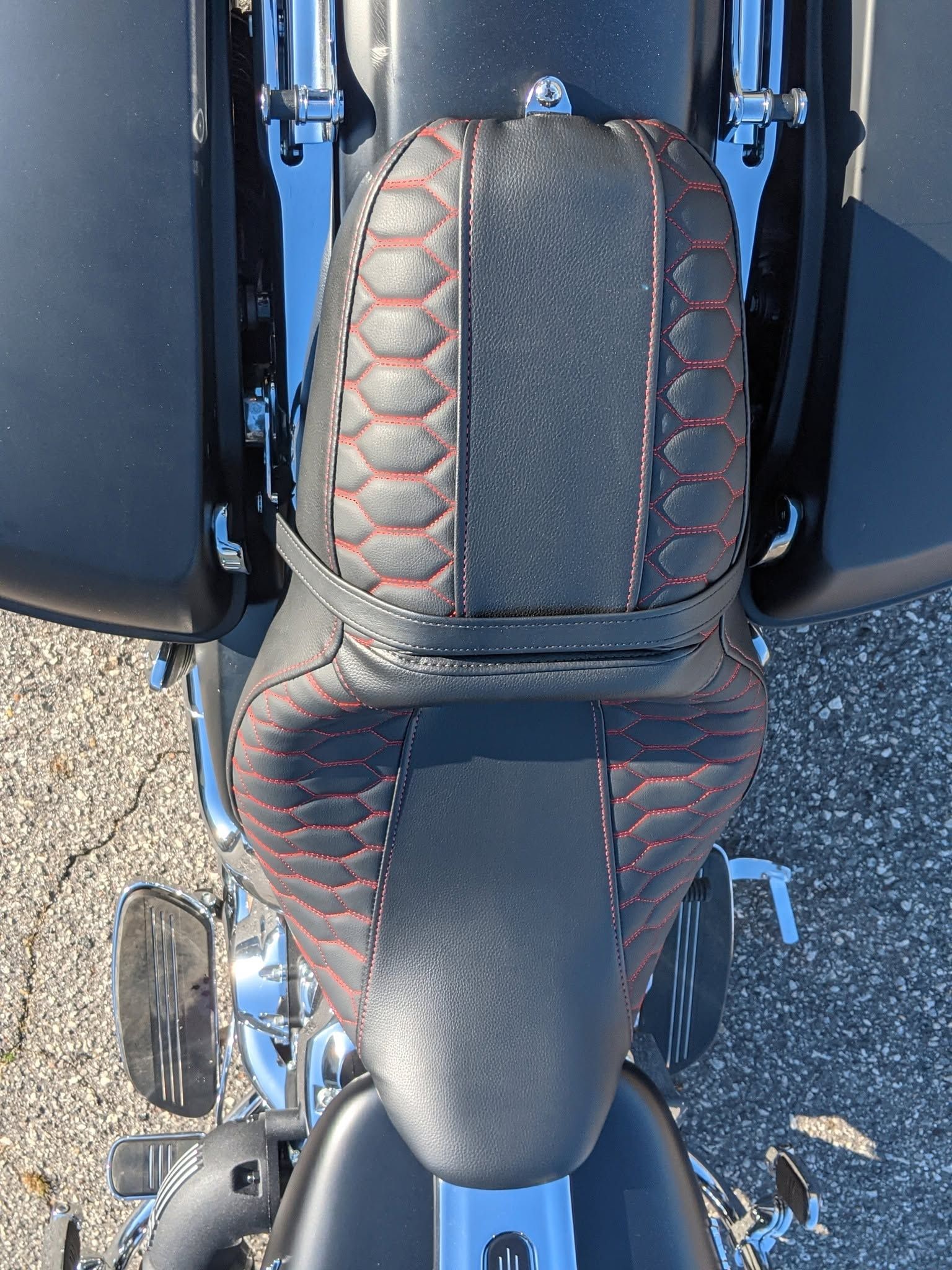 Black quilted motorcycle seat with red stitching viewed from above on a bike.