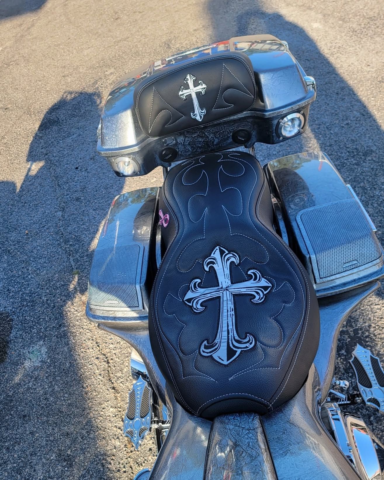 Black motorcycle seat and storage compartments with white cross designs on a sunlit surface