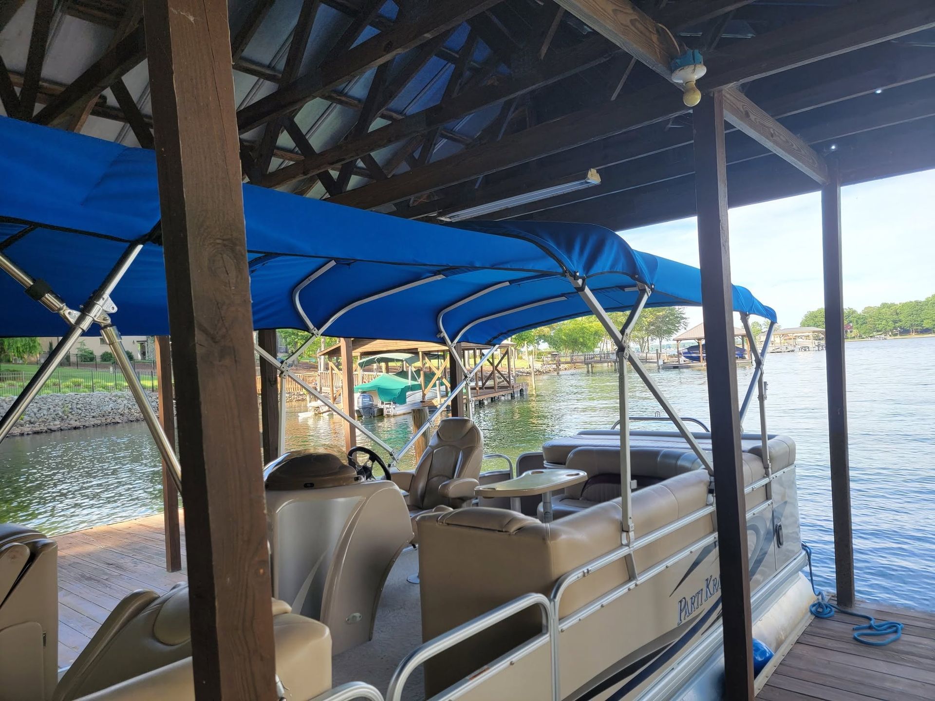 Covered dock with a beige pontoon boat and blue canopy on a lake