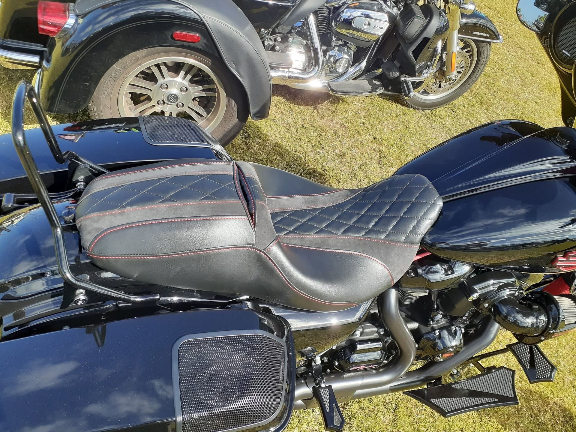 Black motorcycle with quilted seat parked on grass beside a trailer wheel.
