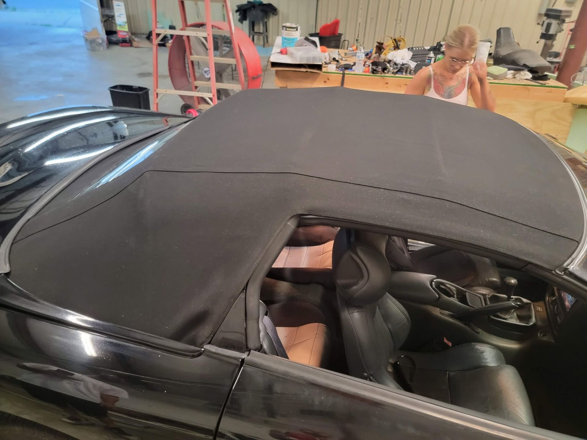 Black convertible top over a sports car in a garage, with the interior visible through the open side.