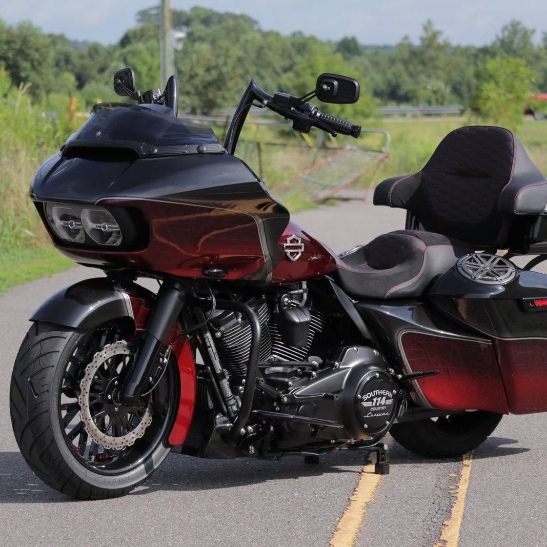 Black and maroon touring motorcycle parked on a road with a scenic green backdrop