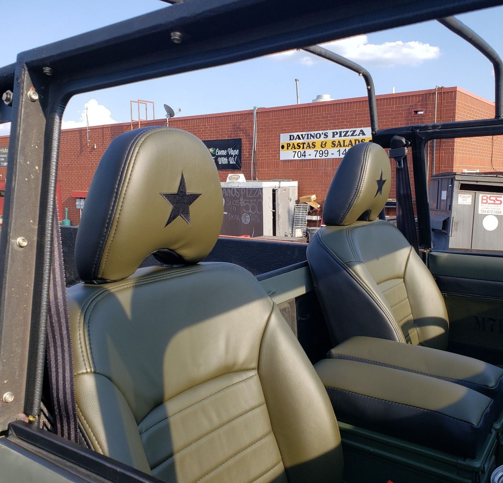 Two tan-and-black bucket seats in an open-top vehicle, with a brick building in the background.