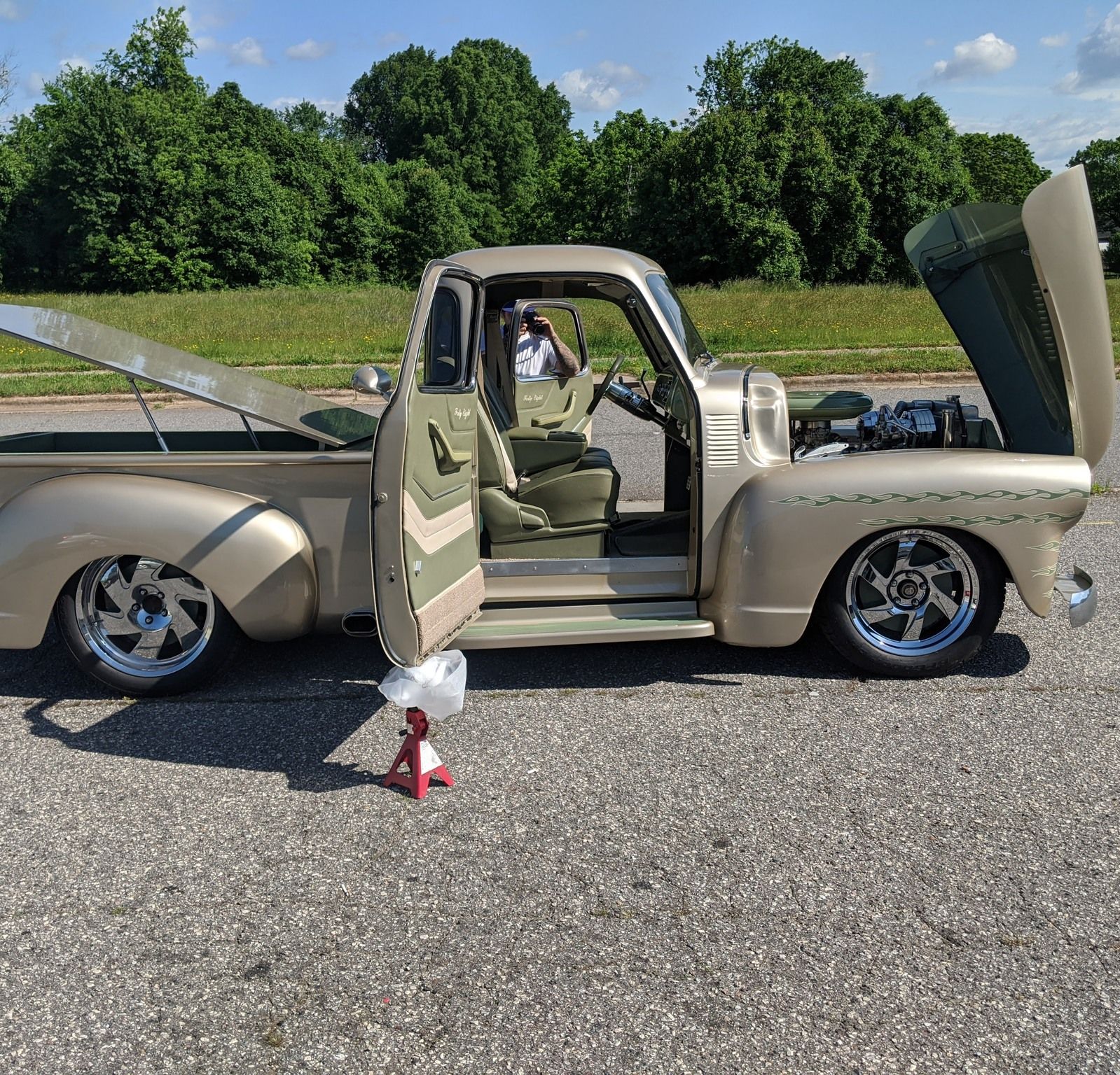 Beige custom vintage pickup truck with open doors and hood, parked on asphalt in bright daylight.