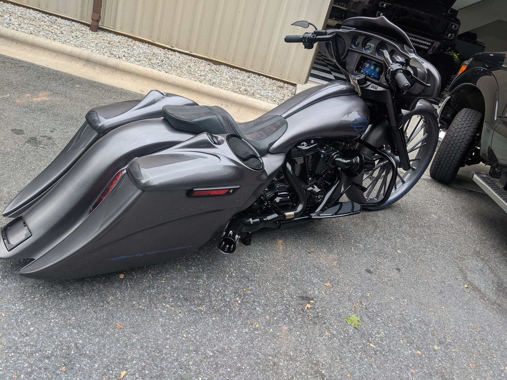 Black motorcycle with large gray saddlebags parked on pavement beside a building