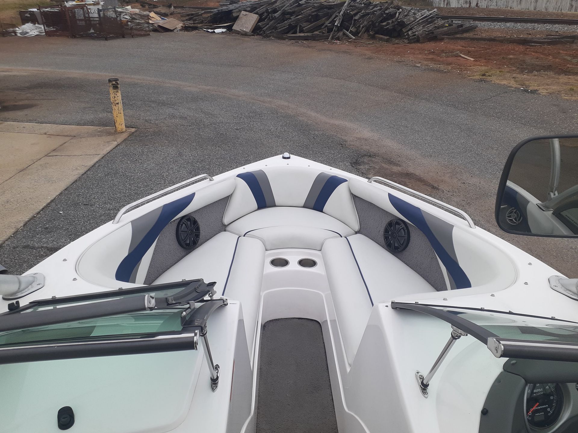Front view from a boat cockpit with white and blue upholstery, parked near a gravel road by the shore.