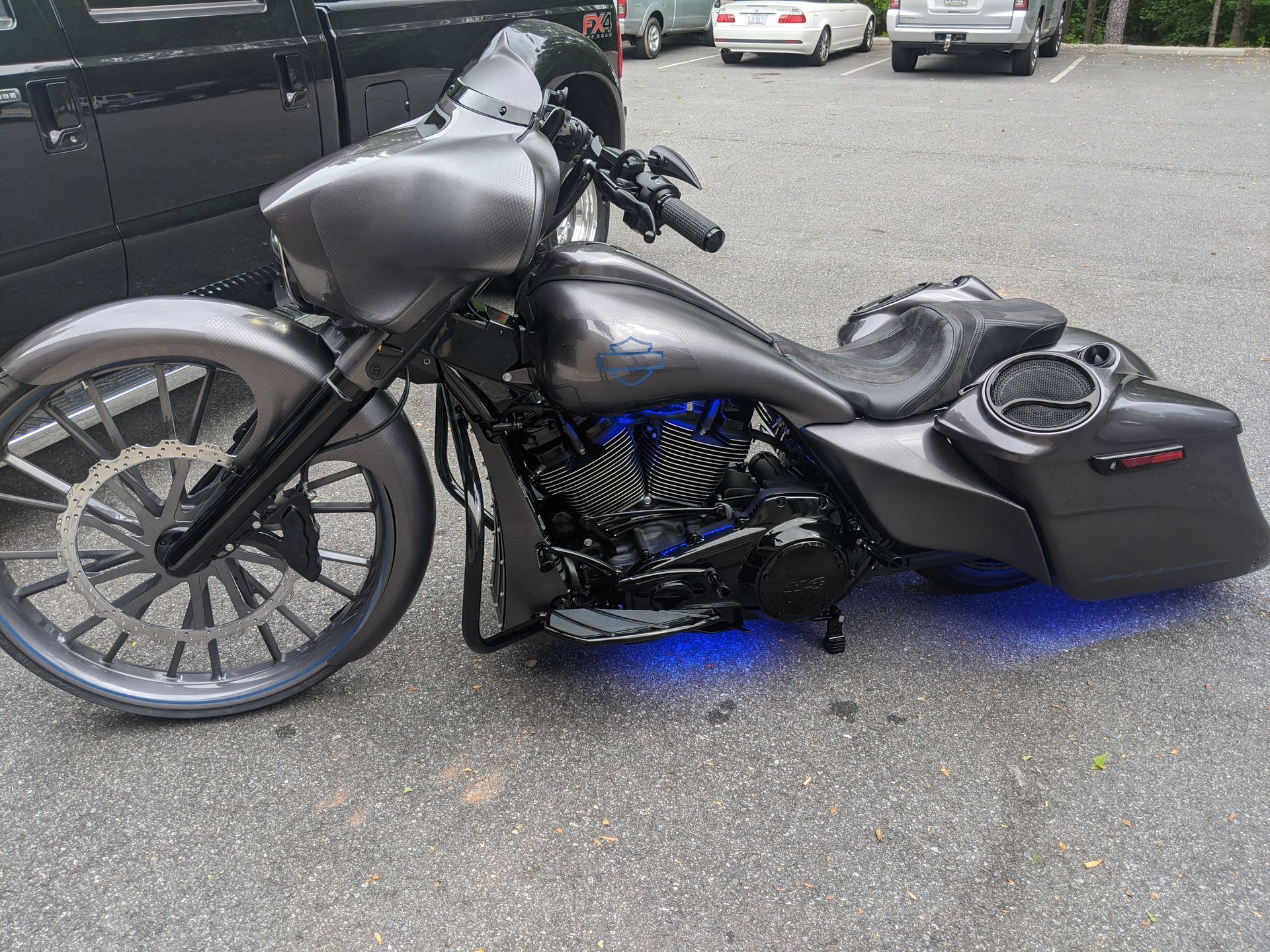 Custom black lowrider motorcycle with blue underglow parked in a lot