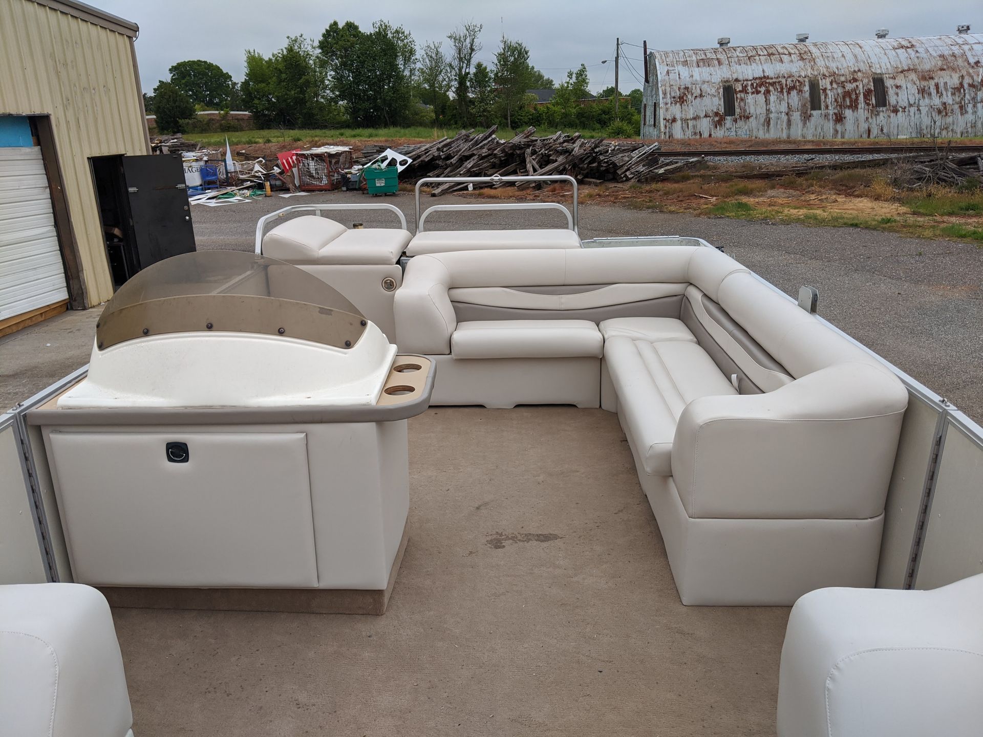 White outdoor sectional sofa set on a concrete patio in a storage yard, with a grill at left.
