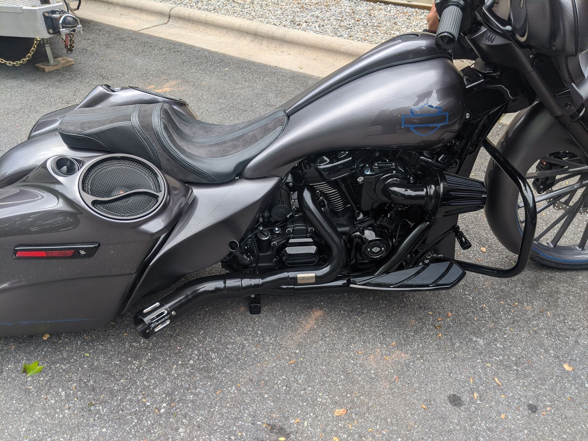 Dark gray custom motorcycle parked on pavement beside a curb, side view