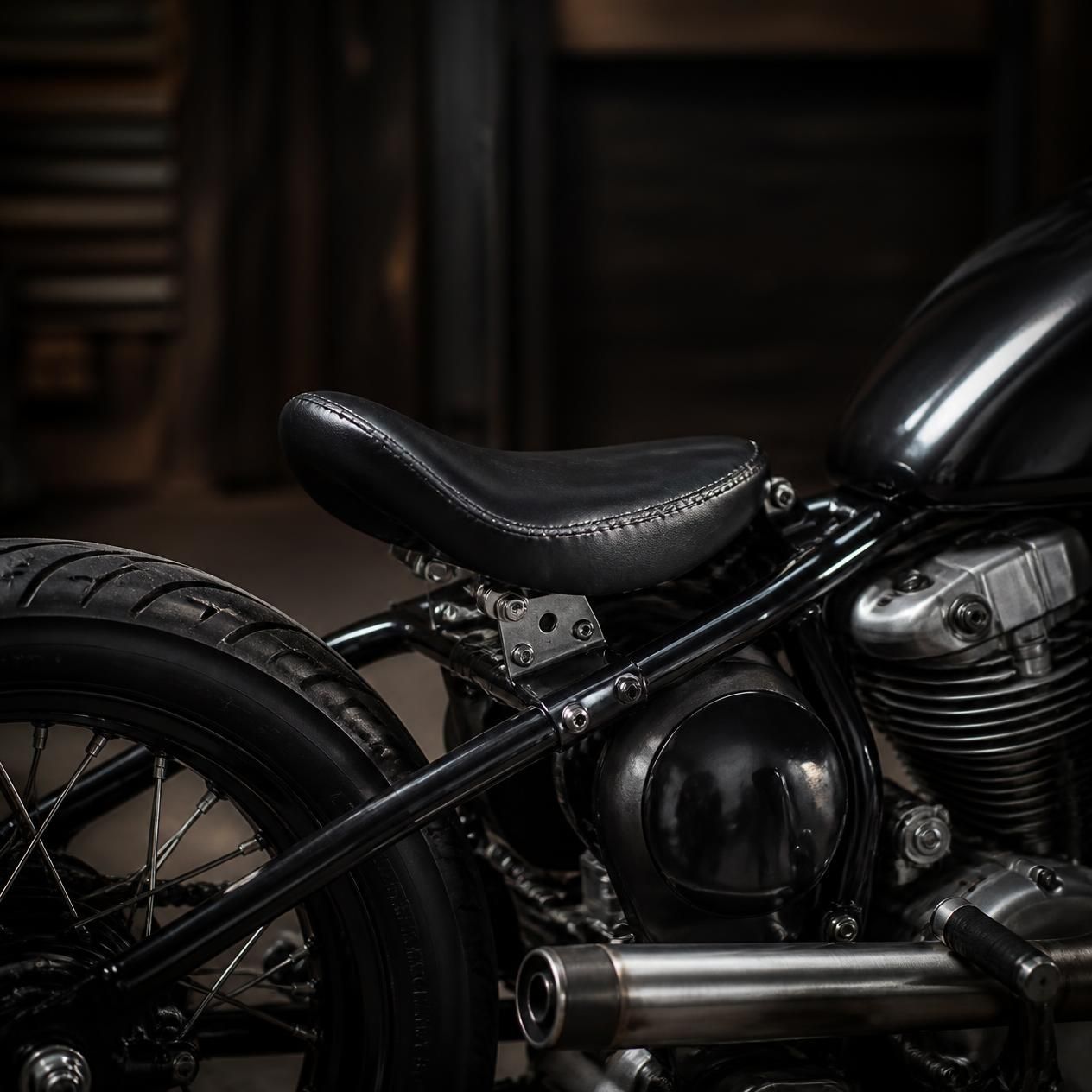 Black motorcycle close-up with leather seat, chrome engine, and rear wheel in a dark garage