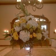Large white and yellow floral arrangement in a church or reception hall on a stand