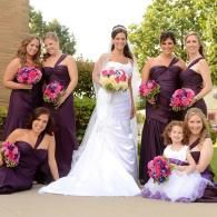 Bride in white gown with bridesmaids in purple dresses holding pink bouquets outdoors