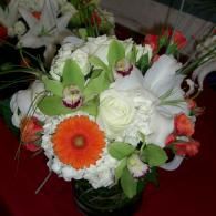 Assorted white, green, and orange flowers arranged in a bouquet on a red surface
