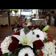 White lilies, red roses, and white daisies in a floral arrangement indoors