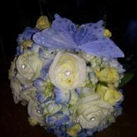 Bouquet of white and pale yellow roses with blue flowers and a lavender butterfly decoration on top