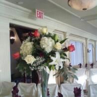 Large white floral arrangement with lilies and roses at a banquet hall entrance
