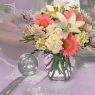 Bouquet of pink gerberas and white roses in a glass vase on a lavender tablecloth with a glass orb and tray