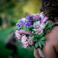 Woman holding a bouquet of pink and purple flowers over her shoulder outdoors