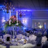 Elegant banquet table with white floral centerpieces and blue uplighting in a decorated ballroom
