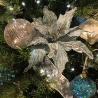 Silver floral ornament with gold and blue baubles on a lit Christmas tree