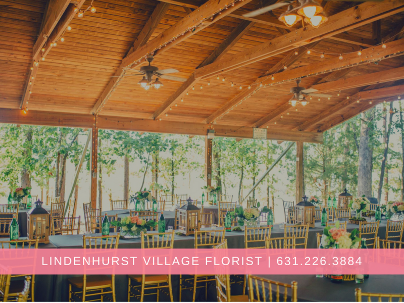 Outdoor reception setup under a wooden pavilion with tables and chairs, surrounded by trees and greenery.