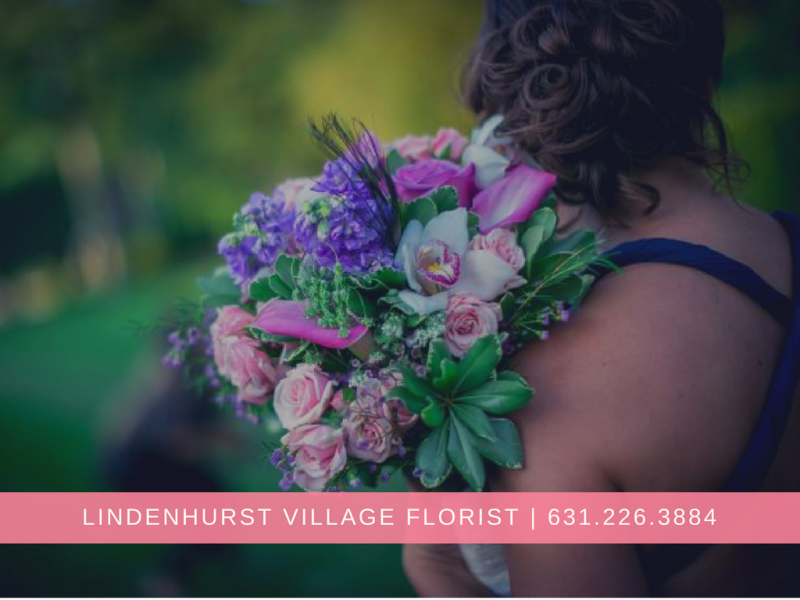 Woman holding a bouquet of purple and pink flowers with green foliage, Lindenhurst Village Florist banner below