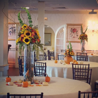 Elegant banquet room with white tablecloths, black chairs, and tall sunflower centerpieces