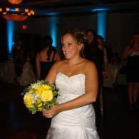 Woman in a white strapless dress holding a yellow bouquet at a dimly lit reception