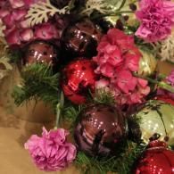 Christmas ornaments and pink flowers arranged with greenery in a decorative display