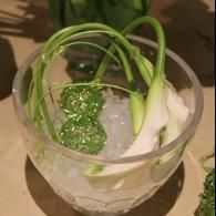 Clear glass bowl with green garlic scapes and ice on a table
