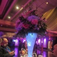 Tall floral centerpiece glowing blue-purple in a dimly lit banquet hall