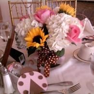 White and pink floral centerpiece in a vase on a set dining table with teacup and plate