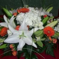White lilies and orange gerberas arranged with white baby's breath in a floral bouquet