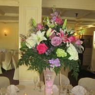Pink, white, and green floral centerpiece in a banquet hall on a table with candles and folded napkins