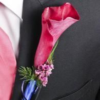 Pink calla lily boutonniere with purple flowers pinned to a black suit lapel