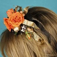 Orange rose hair accessory with gold ribbon on brown hair, against a blue background