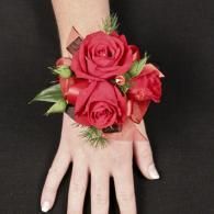 Red rose corsage on a person’s wrist and hand against a black background