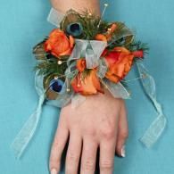 Hand with orange flowers, blue ribbon, and peacock feather wrist corsage on a teal background