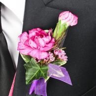 Pink and purple boutonniere with ribbon pinned to a black suit lapel