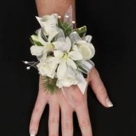 White floral wrist corsage on a person’s hand against a black background